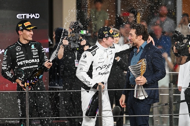 Die Schauspieler Brad Pitt (im weißen Rennanzug) und Javier Bardem auf dem Podium in Abu Dhabi. Links im Bild: Mercedes-Pilot George Russell